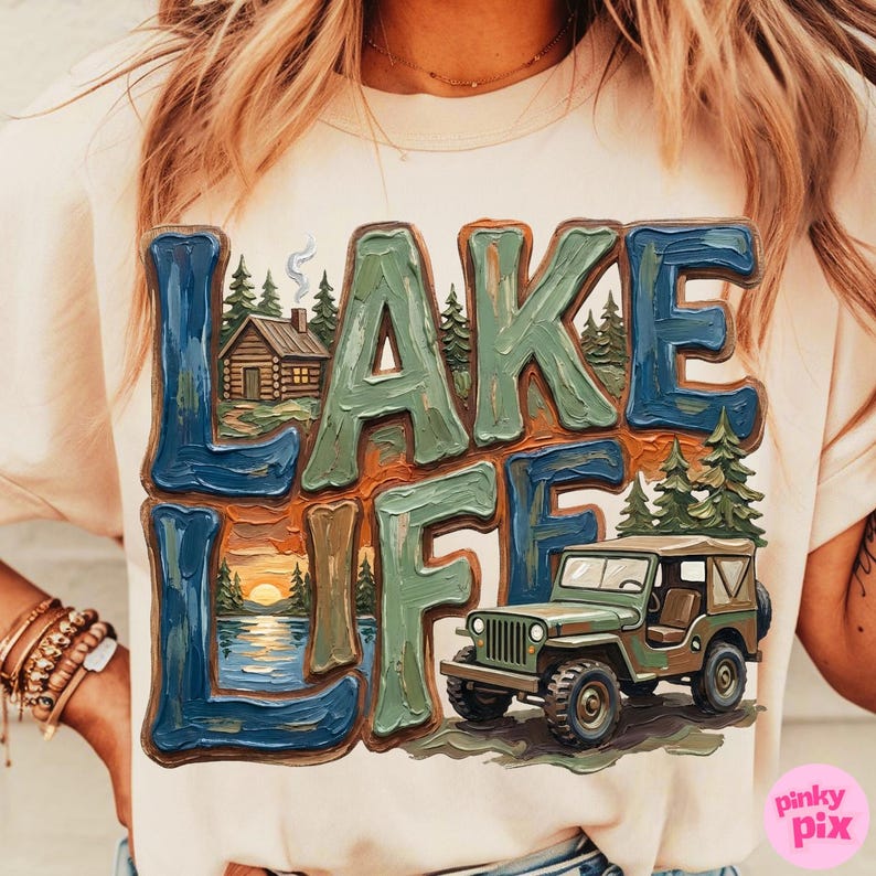 May include: Cream-colored t-shirt with a graphic that says "LAKE LIFE" in blue and green block letters. The graphic includes a cabin, trees, a sunset over a lake, and a green jeep.