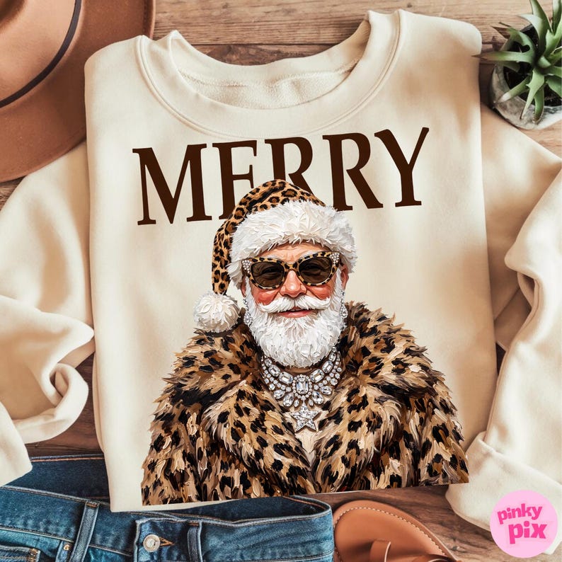 以下が含まれることがあります： クリーム色のクルーネックのスウェットシャツ。ブラウンの文字で「MERRY」と書かれ、その下にヒョウ柄の帽子とコート、サングラスを着用し、星のペンダントが付いた大きなクリスタルのステートメントネックレスを身に着けたサンタクロースのグラフィックがプリントされています。