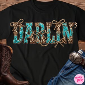 Pu&ograve; includere: T-shirt nera con la scritta "DARLIN" in turchese, stampa leopardata e dettagli in corda. Le lettere hanno un aspetto turchese simile a una pietra, con stampa leopardata e dettagli a stella. Fiocchi di corda sono legati attorno alle lettere.