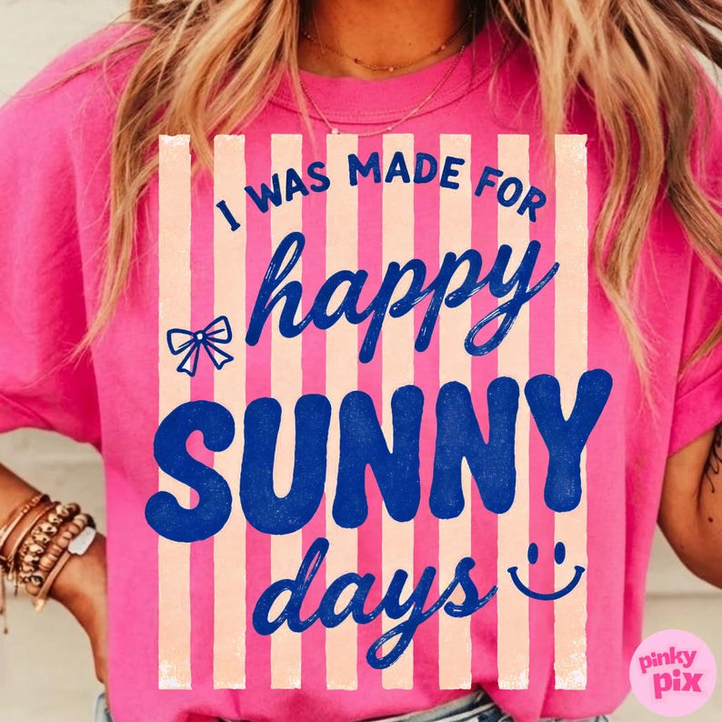 May include: A bright pink t-shirt with the text "I WAS MADE FOR happy SUNNY days" in blue and white. The design includes a bow and a smiling face. The shirt has short sleeves.