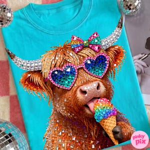 May include: A turquoise t-shirt featuring a whimsical illustration of a Highland cow wearing heart-shaped sunglasses and a bow, with a rainbow ice cream cone. The cow's fur is adorned with sparkling embellishments.