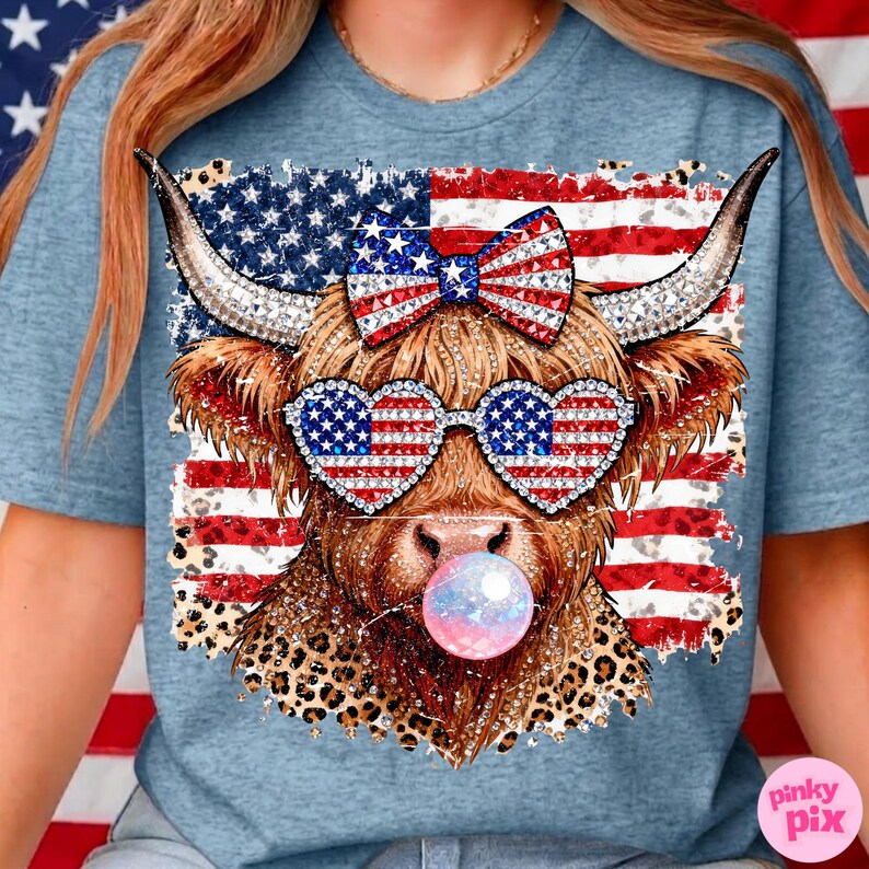 May include: Light blue t-shirt featuring a cow graphic with patriotic sunglasses, a bow, and a bubblegum bubble. The cow is set against a distressed American flag design with a leopard print accent.