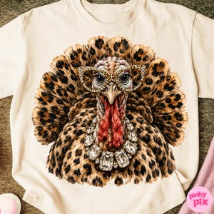 May include: A cream-colored t-shirt featuring a graphic of a turkey with leopard print feathers. The turkey wears leopard print cat-eye glasses and a large, multi-faceted clear crystal statement necklace. The design is centered on the chest.