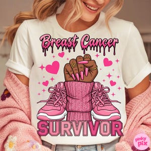 May include: White t-shirt with a pink graphic design. The design includes the words "Breast Cancer Survivor" in a dripping font, a raised fist, pink hearts, and pink sneakers with pink ribbons.