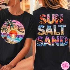 May include: Black t-shirt with a colorful beach scene design. The front features a sunset, palm trees, and the words "Sun Salt Sand" in a circle. The back of the shirt repeats the words "Sun Salt Sand" in a vertical arrangement.