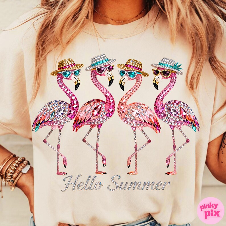 May include: A light beige t-shirt featuring four pink flamingo illustrations. Each flamingo wears sunglasses and a hat. The phrase "Hello Summer" is written in silver glitter below the flamingos. The shirt is a casual summer wear.