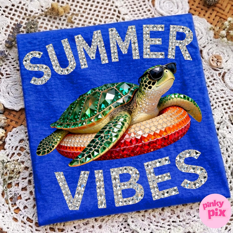 May include: Blue t-shirt with the words "SUMMER VIBES" in silver glitter. A bejeweled turtle wearing sunglasses floats on an inflatable ring. The shirt has a Pinky Pix logo.