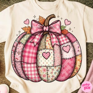 May include: Cream-colored t-shirt featuring a patchwork pumpkin design. The pumpkin is composed of various pink patterns, including gingham and floral prints, with a pink bow and heart accents. The design has a stitched appearance.