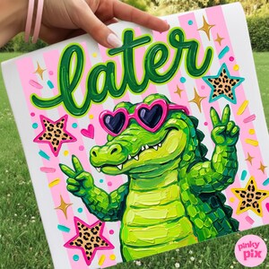 May include: A colorful artwork featuring a green alligator wearing heart-shaped sunglasses and giving a peace sign. The word "later" is written in green script above the alligator. Pink and white stripes form the background, with star and heart accents.