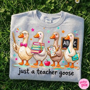 May include: A light gray sweatshirt featuring four cartoon geese dressed as teachers. One goose holds a pointer, another books, a third a clipboard, and the last a chalkboard. The text "just a teacher goose" is below the geese.