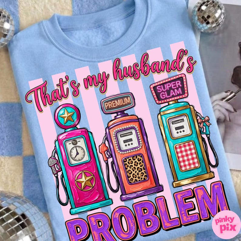 May include: Light blue sweatshirt with a graphic of three vintage gas pumps in pink, orange, and teal. Text reads "That's my husband's problem" in pink and purple. The design includes the text "Premium" and "Super Glam".