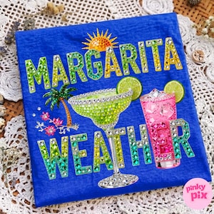 Peut inclure: T-shirt bleu avec l'inscription &laquo; Margarita Weather &raquo; en lettres serties de bijoux. Le motif comprend un verre &agrave; margarita orn&eacute; de bijoux, un cocktail rose, un soleil, un palmier et des tranches de citron vert.