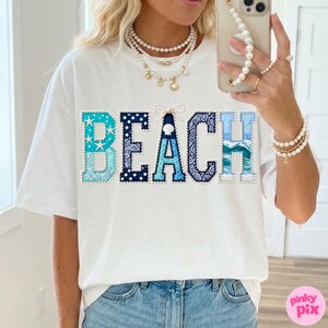 May include: White t-shirt with the word "BEACH" in blue, patterned letters. The "B" is light blue with starfish, the "E" is navy with polka dots, the "A" is navy with a paisley design, the "C" is light blue with a wave pattern, and the "H" is light blue.