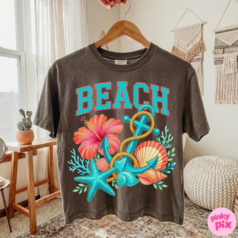 May include: A dark grey t-shirt featuring the word "BEACH" in turquoise lettering. The design includes a turquoise anchor, rope, a pink hibiscus flower, a blue starfish, and seashells.