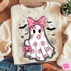 May include: Cream-coloured sweatshirt with a cute ghost design. The ghost has a pink bow and holds a pumpkin bucket. Decorated with pink pumpkins and black lace trim, with bats, spiders, and spiderwebs for a Halloween theme.