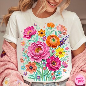 May include: White t-shirt featuring a vibrant floral design. The design includes large pink peonies, orange ranunculus, and various other colorful flowers. The shirt has short sleeves and a crew neck, perfect for a casual look.