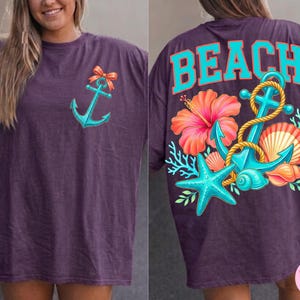 May include: A purple t-shirt with a teal anchor graphic and orange bow on the front. The back features the word "BEACH" in teal, along with a floral and nautical design including an anchor, starfish, and seashell.