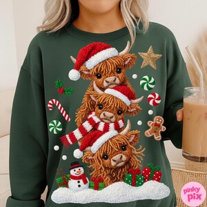 May include: Dark green sweatshirt featuring a stacked design of three Highland cows wearing Santa hats and a scarf. Festive elements include a snowman, gifts, candy canes, and a gingerbread man. The design is a cozy, holiday-themed graphic.