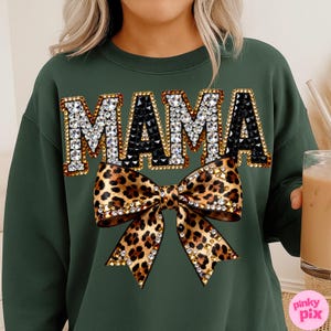May include: A dark green sweatshirt with the word "MAMA" in large, jeweled letters. Below the text is a leopard print bow with crystal embellishments. The sweatshirt is a casual, stylish garment.