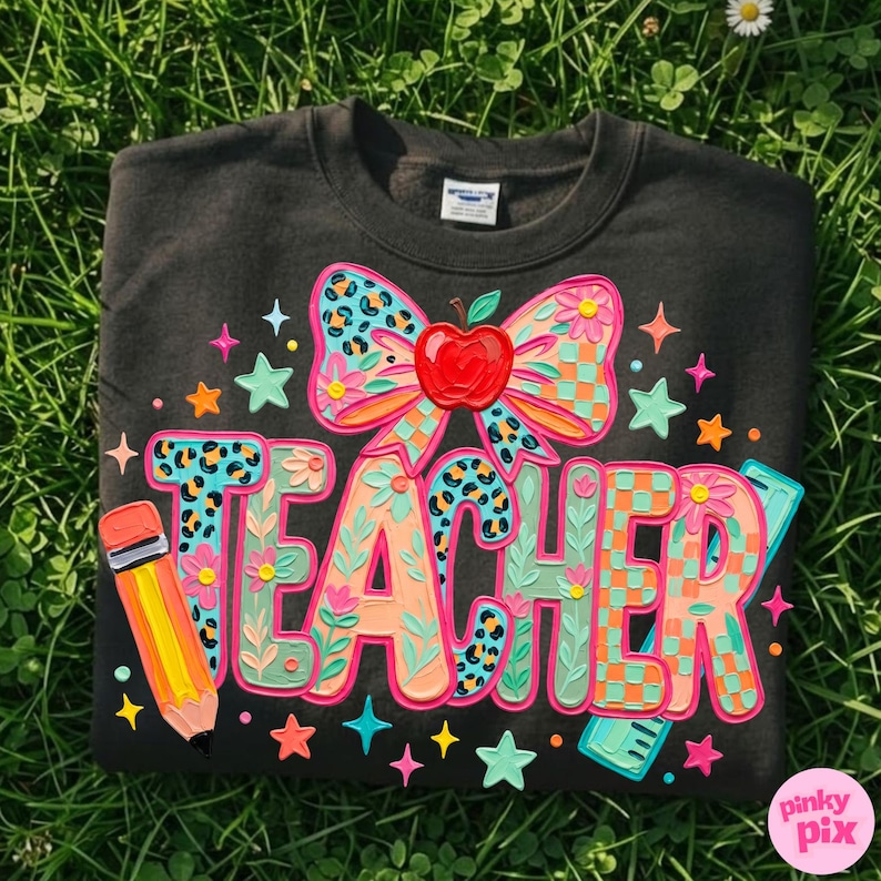 May include: Black sweatshirt with a colorful "TEACHER" design. The design includes a bow with a red apple, stars, a pencil, and a ruler. The letters are in various patterns and colors, including teal, orange, and pink.