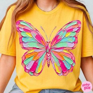 May include: Yellow t-shirt featuring a vibrant, textured butterfly design. The butterfly has wings in shades of pink, green, orange, and purple. The shirt is a solid yellow color, and the butterfly design is centered on the front.