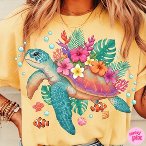 May include: Yellow t-shirt featuring a colorful sea turtle design. The turtle is adorned with tropical flowers and surrounded by bubbles, coral, and fish. The design includes pink, orange, blue, and green elements.