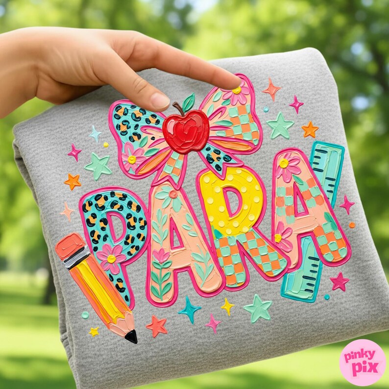 May include: A gray sweatshirt with the word "PARA" in colorful, textured letters. The design includes a bow with an apple, a pencil, a ruler, and star accents. The design is in bright colors.