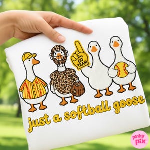 May include: White sweatshirt featuring four cartoon geese dressed in baseball and softball gear. One goose wears a baseball uniform, another a catcher's outfit, and the third holds a foam finger. The text "just a softball goose" is printed in yellow.