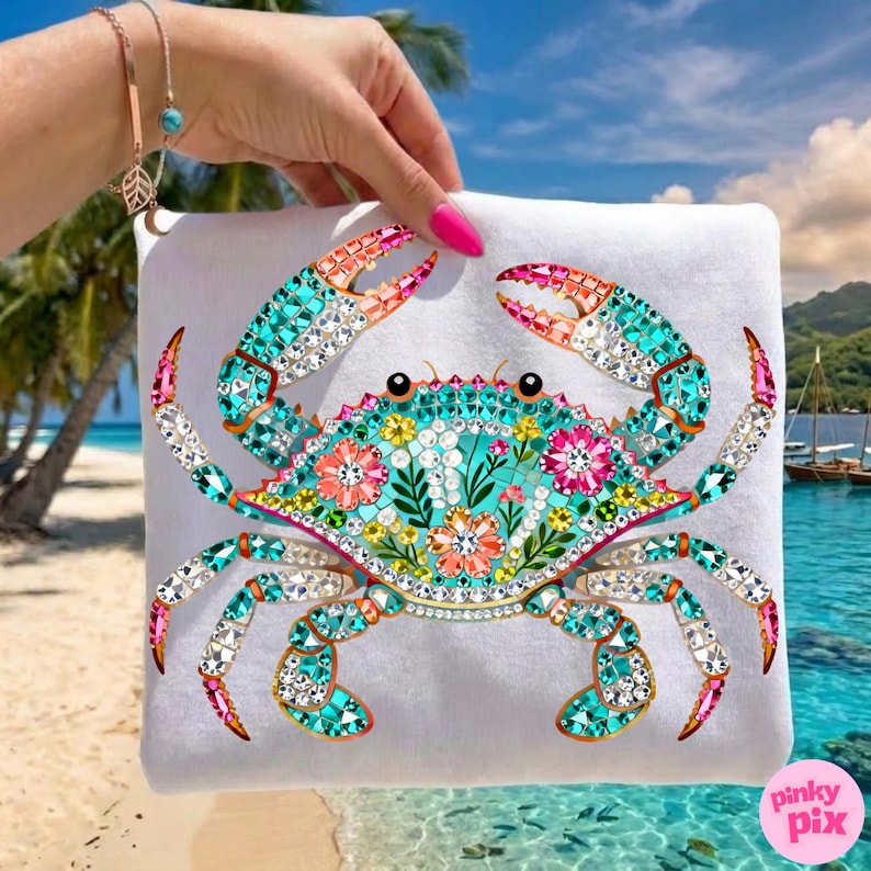 May include: White square pillow featuring a colorful crab design. The crab is decorated with turquoise, pink, and clear crystals, and floral accents. The background shows a tropical beach scene with palm trees and ocean.