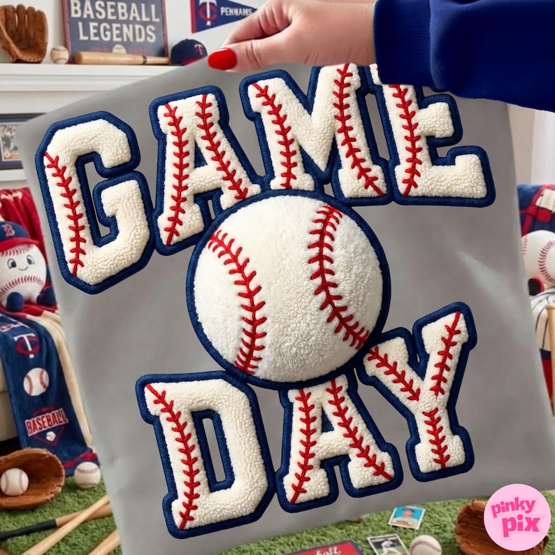 May include: A gray baseball-themed pillow with the words "GAME DAY" in white, fluffy letters with red stitching and blue trim. A baseball is in the center. The pillow is surrounded by baseball-related items.