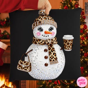 May include: Black square pillow featuring a mosaic-style snowman with a leopard print hat, scarf, and purse. The snowman has a carrot nose, pink cheeks, and is holding a leopard print coffee cup. The pillow is held by a person.