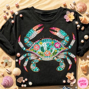 May include: Black long-sleeve shirt featuring a detailed, jewel-toned crab design. The crab is adorned with turquoise, pink, and white gems, and floral accents. The design is centered on the shirt, with a crew neck and long sleeves. The shirt is surrounded by seashells and pearls.