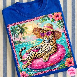 May include: Royal blue t-shirt with a colourful illustration of a leopard wearing sunglasses and a straw hat, floating on a pink inflatable ring in the sea. The design includes palm trees, flowers, and a beach scene.