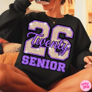 May include: Black sweatshirt with a glittery design featuring the number "26", the word "Twenty" in script, and the word "SENIOR" in purple block letters. The design has a purple and gold color scheme.
