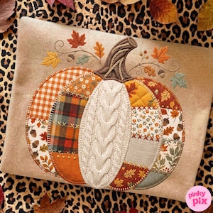May include: A beige sweatshirt featuring a large, central pumpkin applique made of various fabric patches including orange gingham, plaid, floral, and cream cable knit. The pumpkin is accented with embroidered autumn leaves and acorns.
