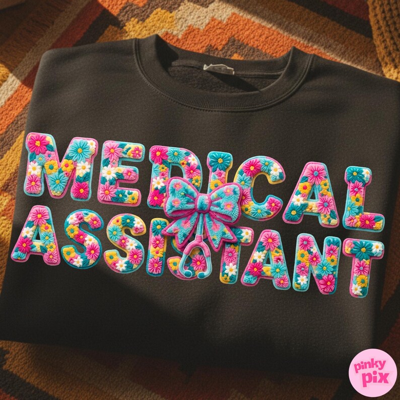 May include: Black sweatshirt with the words "MEDICAL ASSISTANT" in colorful floral letters. A bow and stethoscope graphic are also included. The design features pink, blue, yellow, and white flowers. The brand name "pinky pix" is in the bottom right corner.