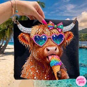 May include: Black square beach towel featuring a rhinestone-covered Highland cow wearing heart-shaped sunglasses and a bow. The cow is licking a rainbow ice cream cone. The background shows a tropical beach scene.