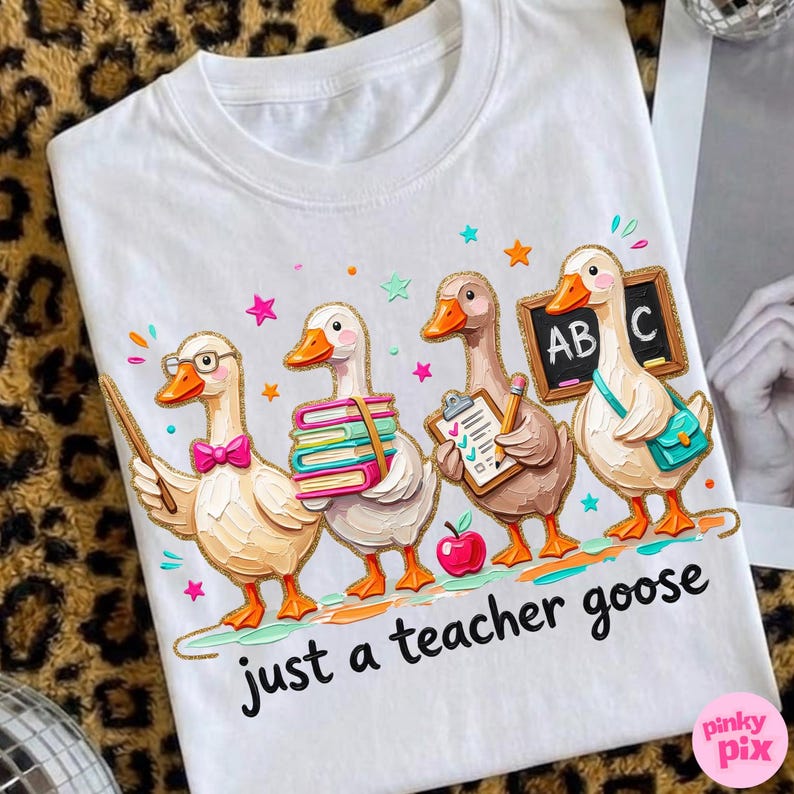 May include: White t-shirt featuring a whimsical illustration of four geese dressed as teachers. Each goose holds school-related items like books, a chalkboard, and a clipboard. The text "just a teacher goose" is printed below the geese.