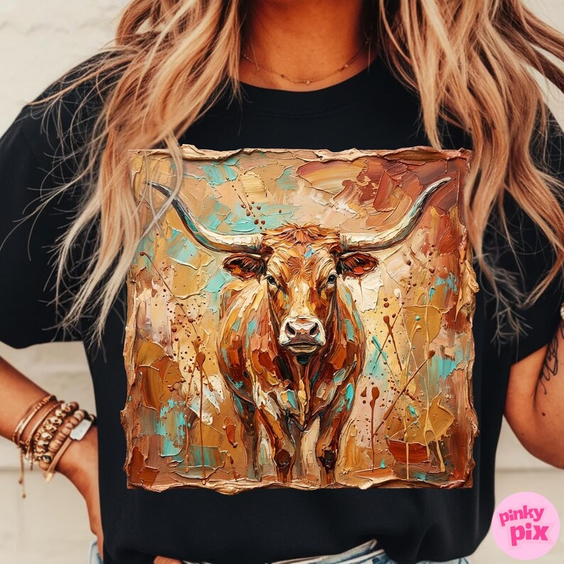 May include: Black t-shirt featuring a detailed, textured painting of a longhorn steer. The artwork uses a palette of browns, golds, and turquoise, with visible brushstrokes and paint splatters, creating a rustic, artistic aesthetic.