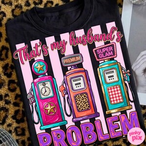 May include: Black t-shirt with a graphic of three vintage gas pumps in pink, teal, and orange, with the text "That's my husband's problem" in pink and purple. The pumps have star and leopard print details.