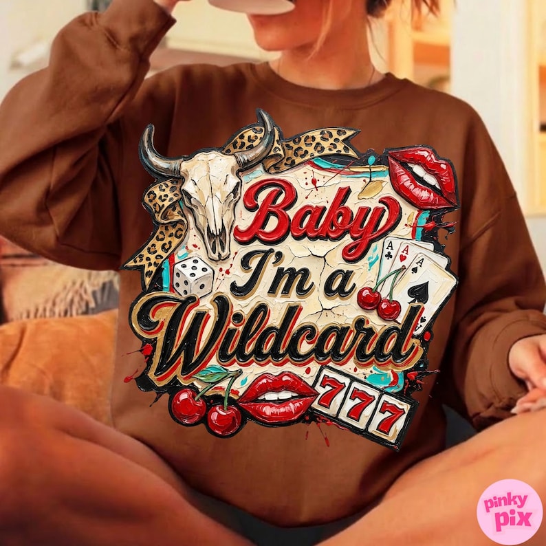 Może przedstawiać: Brązowa bluza z nadrukiem przedstawiającym czaszkę byka, karty do gry, wiśnie, kostki do gry oraz napis "Baby I'm a Wildcard". Projekt zawiera czerwone usta i liczbę 777.