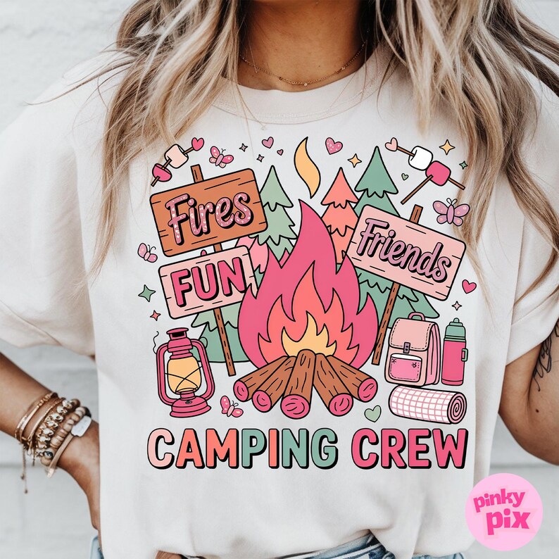 May include: Beige t-shirt with a colorful camping-themed graphic. The design includes a campfire, trees, and signs that read "Fires," "Fun," and "Friends." The words "Camping Crew" are also displayed.