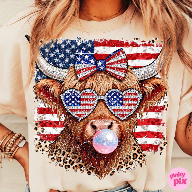 May include: A beige t-shirt featuring a graphic of a Highland cow with patriotic sunglasses and a bow, both adorned with the American flag. The cow is blowing a bubblegum bubble. The design includes a leopard print pattern.