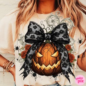May include: A beige t-shirt featuring a Halloween-themed graphic. The design includes a carved orange pumpkin with a black lace bow, red roses, and spider accents. The text "pinky pix" is visible in the lower right corner.