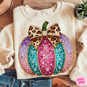 Op de afbeelding: Een cr&egrave;mekleurige sweater met ronde hals en een grote afbeelding van een pompoen versierd met veelkleurige strass-steentjes in roze, paarse en turquoise tinten. De pompoen is afgewerkt met een strik met luipaardprint en stervormige steentjes.