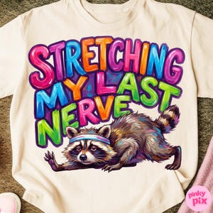 May include: Cream-colored t-shirt with the text "STRETCHING MY LAST NERVE" in colorful bubble letters. A raccoon wearing a headband is stretching. The raccoon is brown, gray, and white.