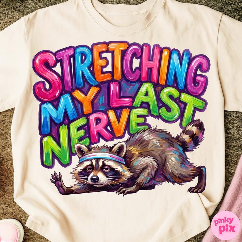 May include: Cream-colored t-shirt with the text "STRETCHING MY LAST NERVE" in colorful bubble letters. A raccoon wearing a headband is stretching. The raccoon is brown, gray, and white.