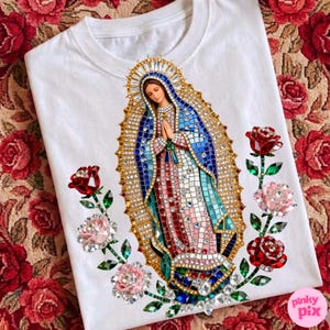 May include: White t-shirt featuring a detailed, jeweled depiction of the Virgin Mary. The design includes blue, pink, and gold accents, surrounded by jeweled roses in red and pink. The shirt has a crew neck.