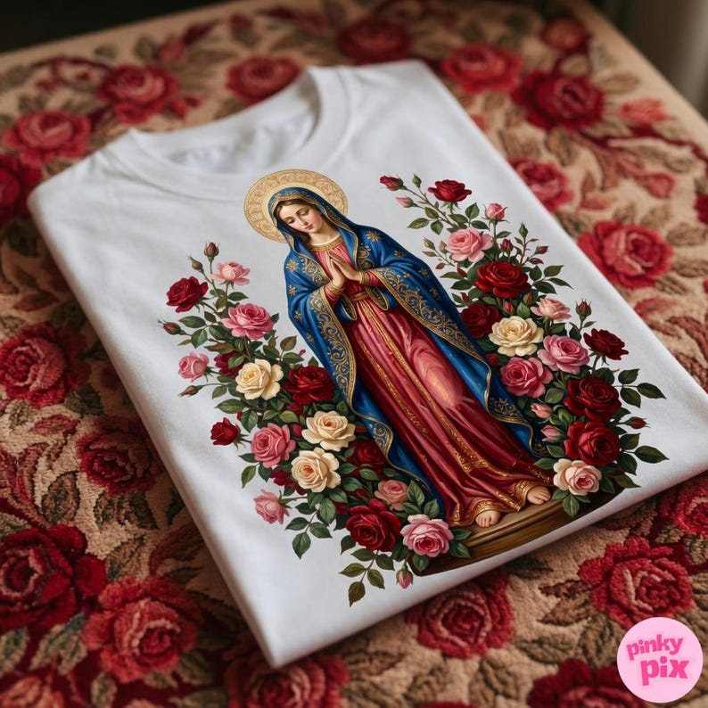 May include: White t-shirt featuring a religious illustration of a woman in a blue and red robe, surrounded by red, pink, and cream roses. The image has a gold halo and is set against a floral background.