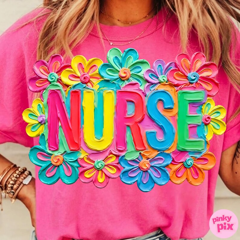 May include: A pink t-shirt with the word "NURSE" in colorful, 3D-style letters, surrounded by vibrant, multi-colored flowers. The shirt is a solid pink color.